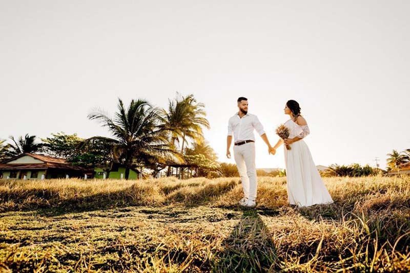 Bride and groom walking at sunset holding hands with wedding photographer capturing the moment
